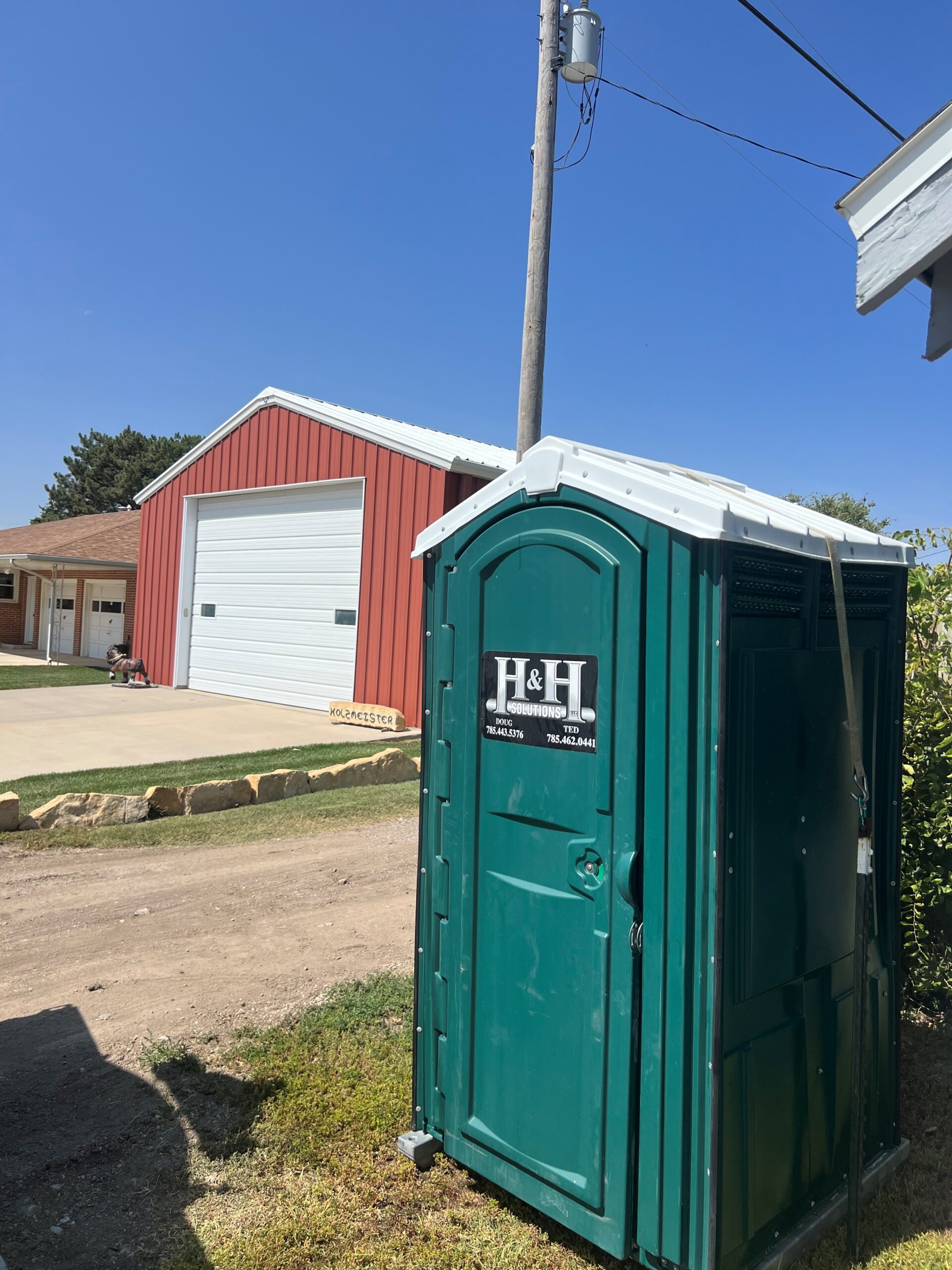 Green rented porta potty green portable toilet in front of a red barn in western kansas